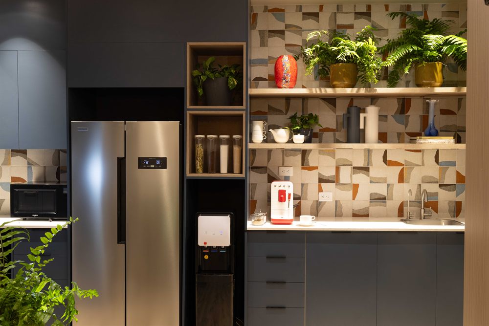 Kitchenette con muebles azul oscuro, estantes abiertos y revestimiento cerámico de piezas en tonos tierra