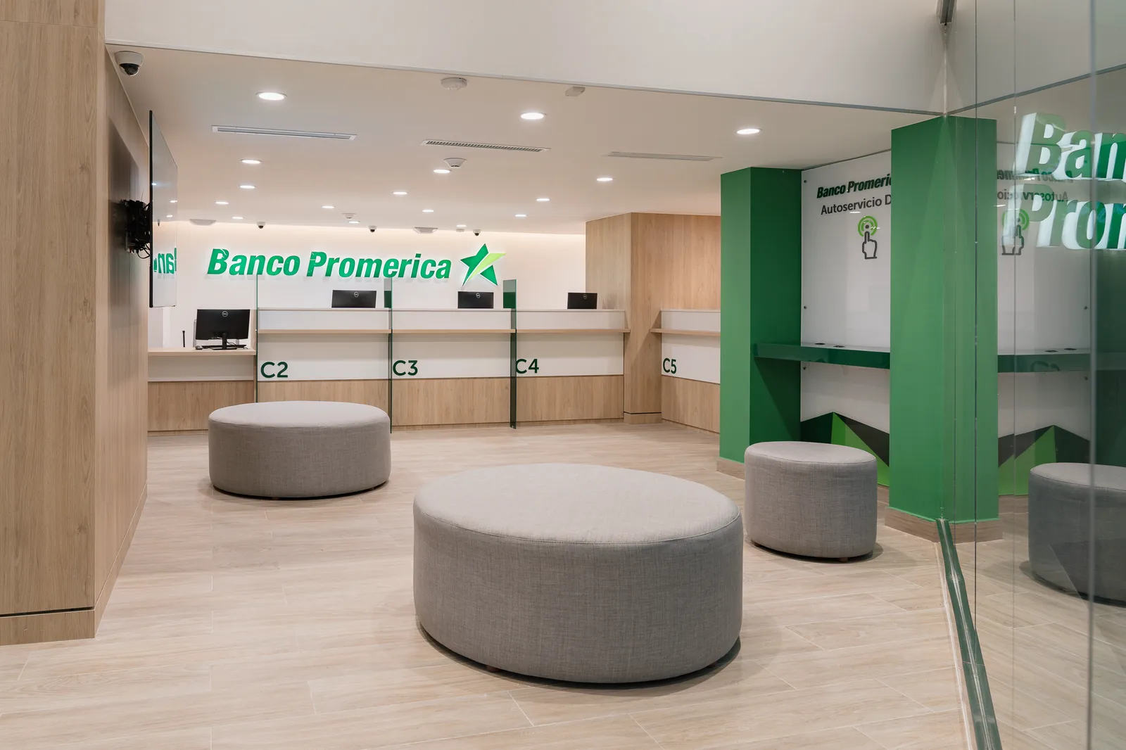 Línea de caja terminada: cuatro puestos numerados bajo el rótulo del banco, frente de madera, plano verde a la derecha y asientos redondos en el área de espera