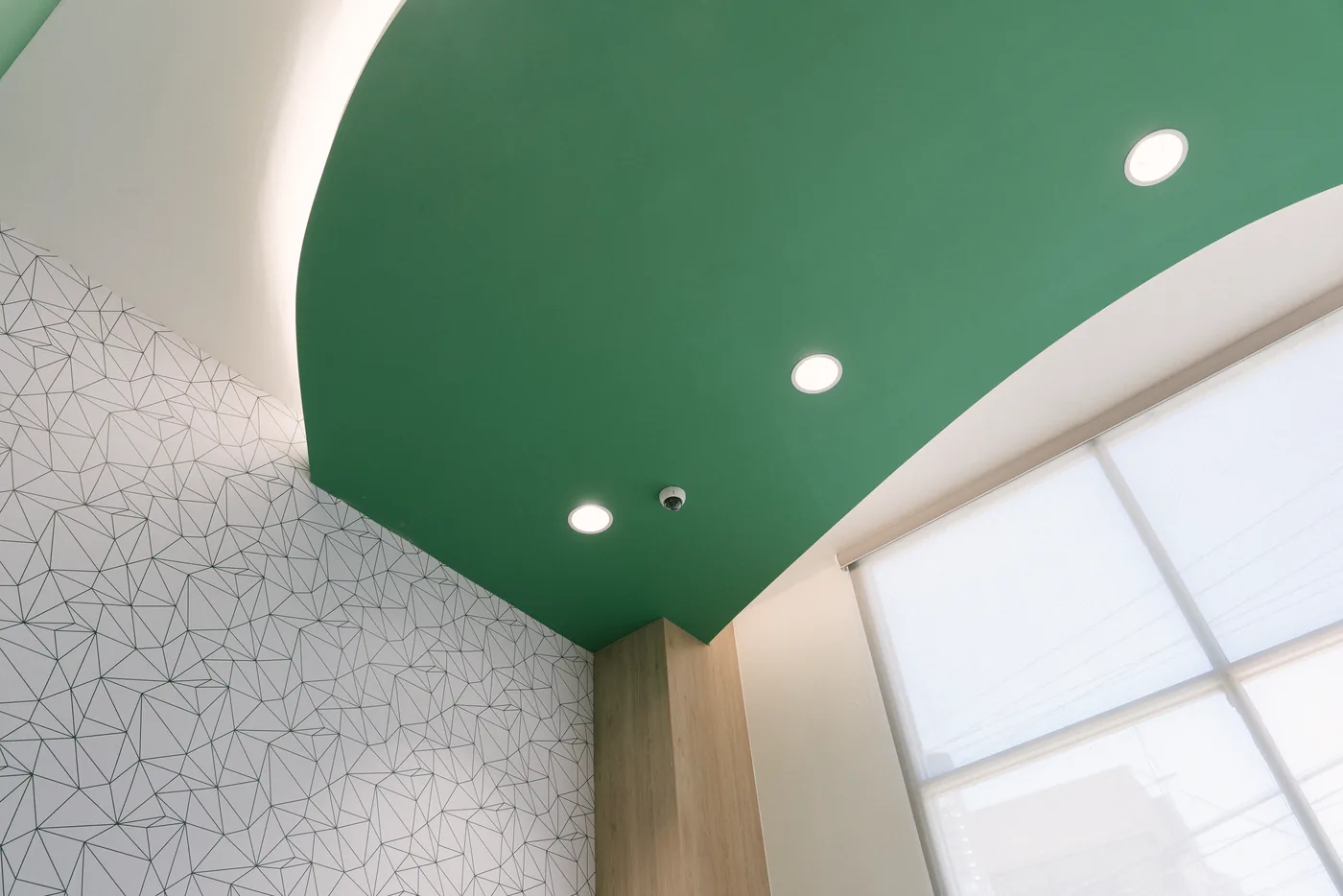 Detalle del encuentro entre el plafón curvo verde, el plano blanco del techo y el muro con el mural de líneas