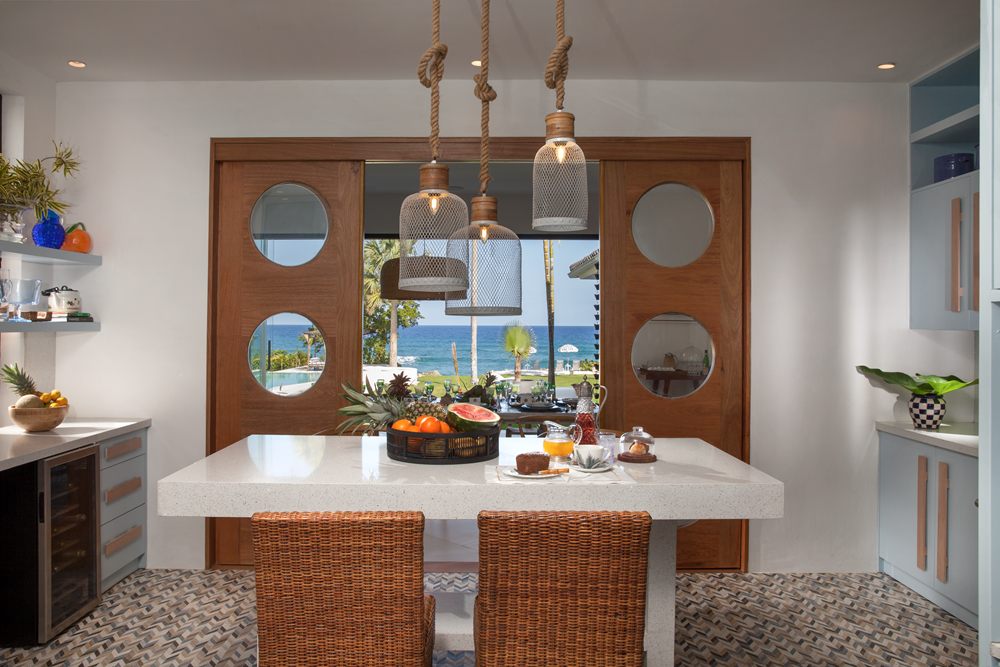 Cocina con una isla blanca frente a dos paneles con ojos de buey; entre ellos, la vista al jardín y al mar