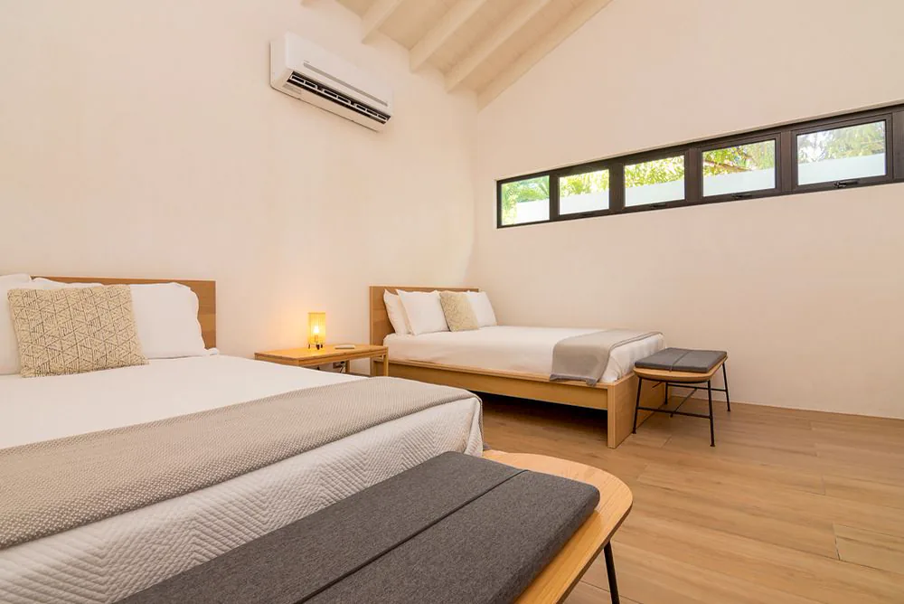 Habitación con una ventana corrida alta sobre el cabecero, banqueta a los pies de la cama y piso de madera clara